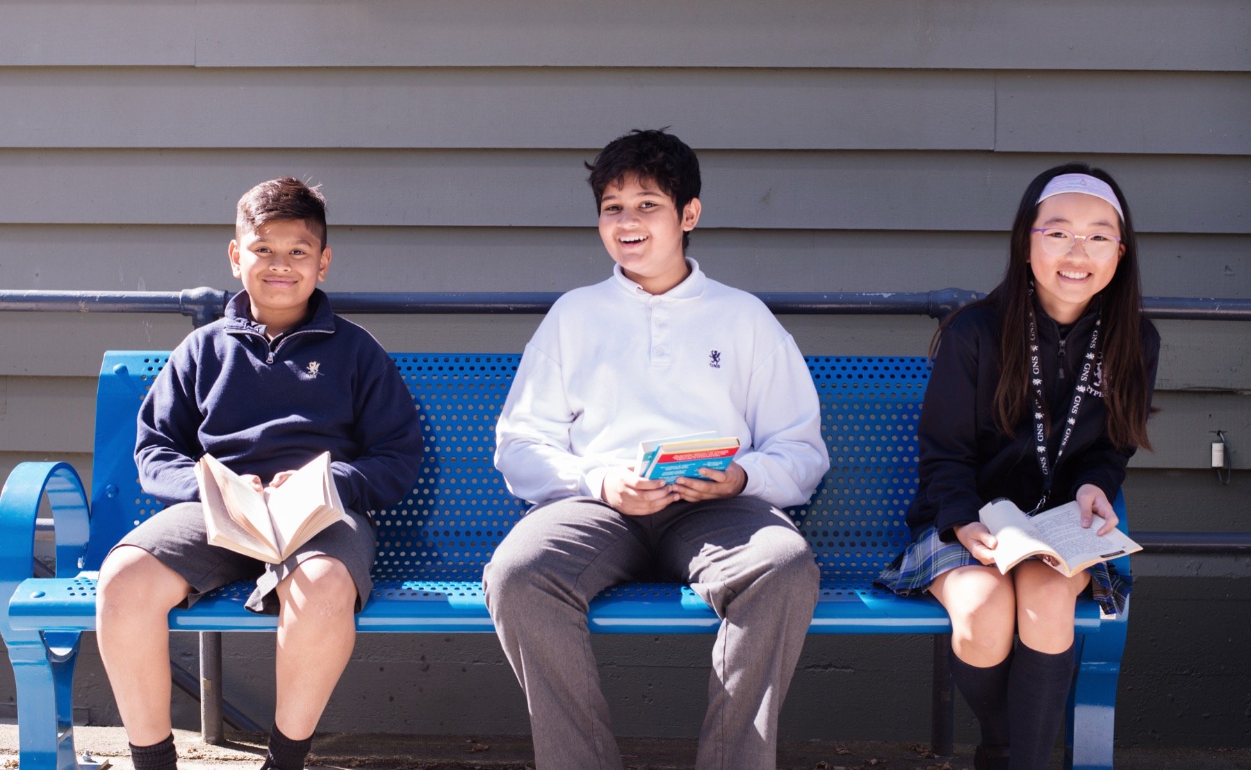 3 gns students sitting on bench reading books