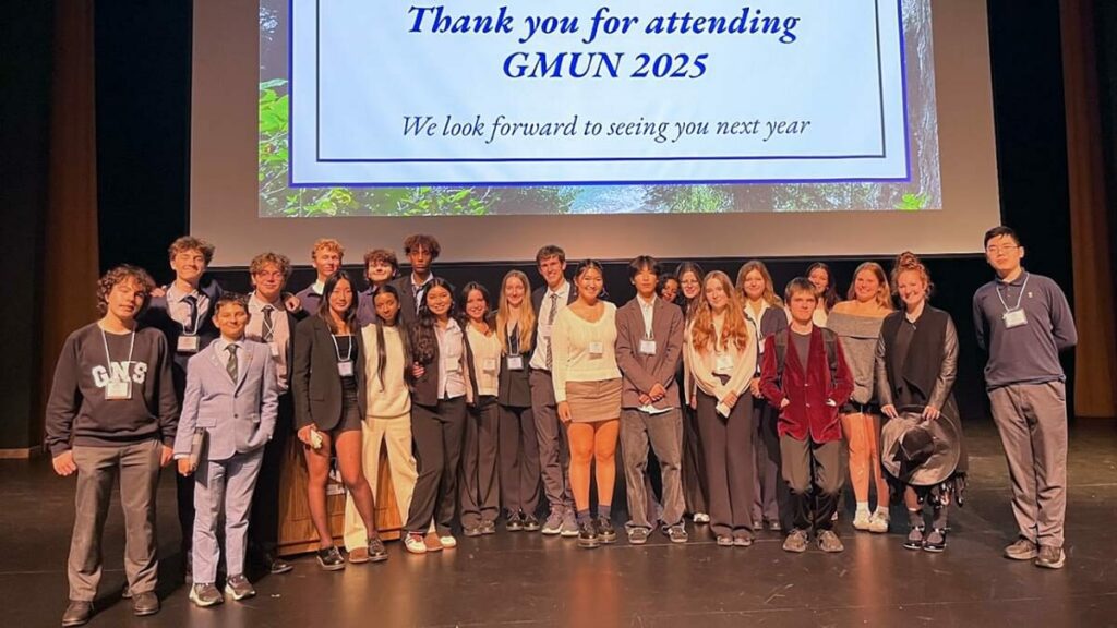 Group photo of student delegates and organizers on stage at the closing of GMUN 2025, with a screen reading “Thank you for attending GMUN 2025.”