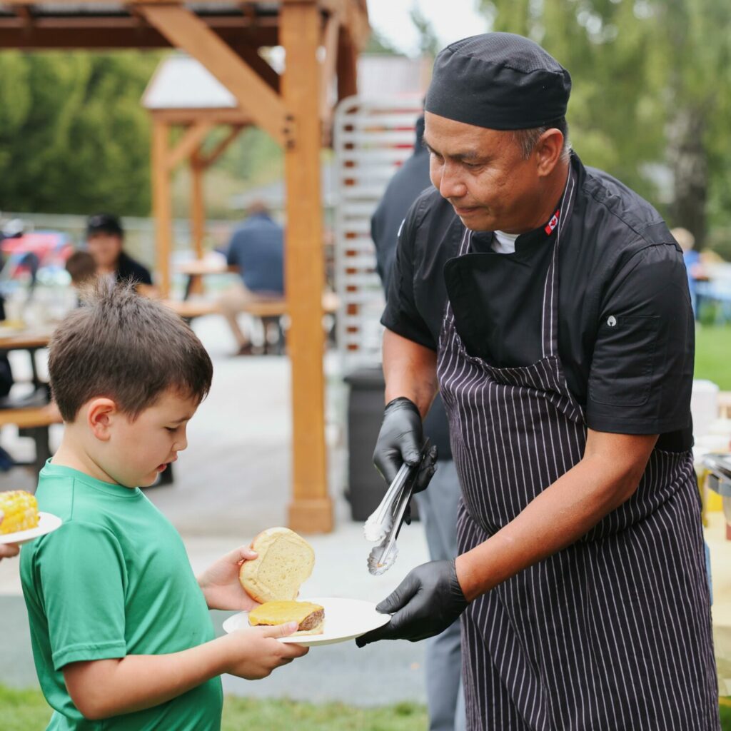 GNS chef serves a hamburger to a young boy during the Family Carnival community barbecue.